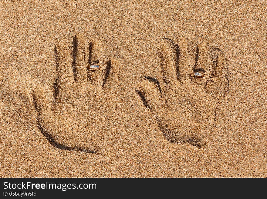 Hand prints on the sand. Hand prints and wedding rings.