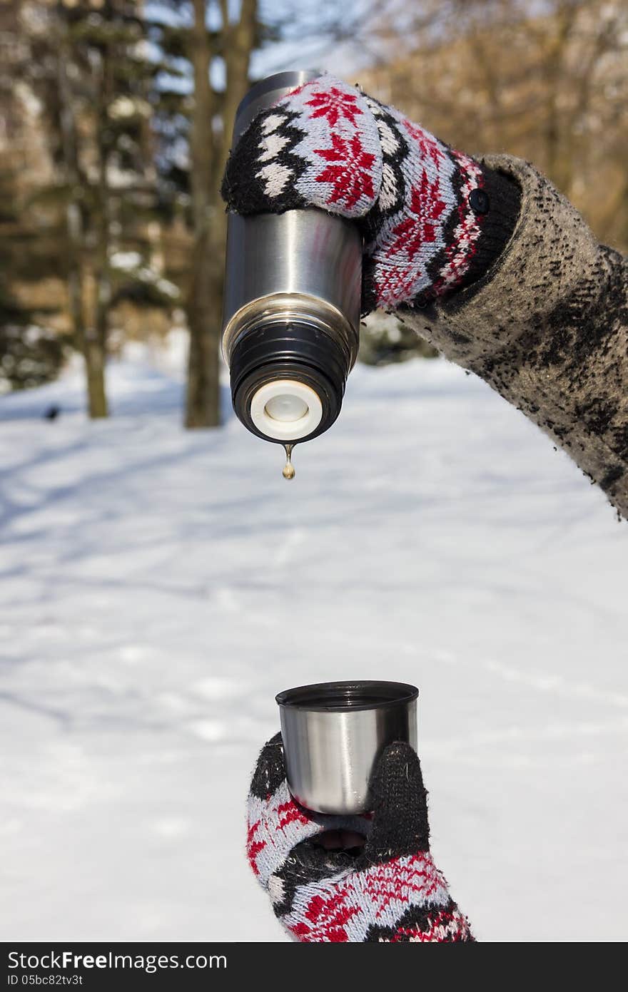 Thermos with the last tea drop and a cup in hands in mittens in winter. Thermos with the last tea drop and a cup in hands in mittens in winter