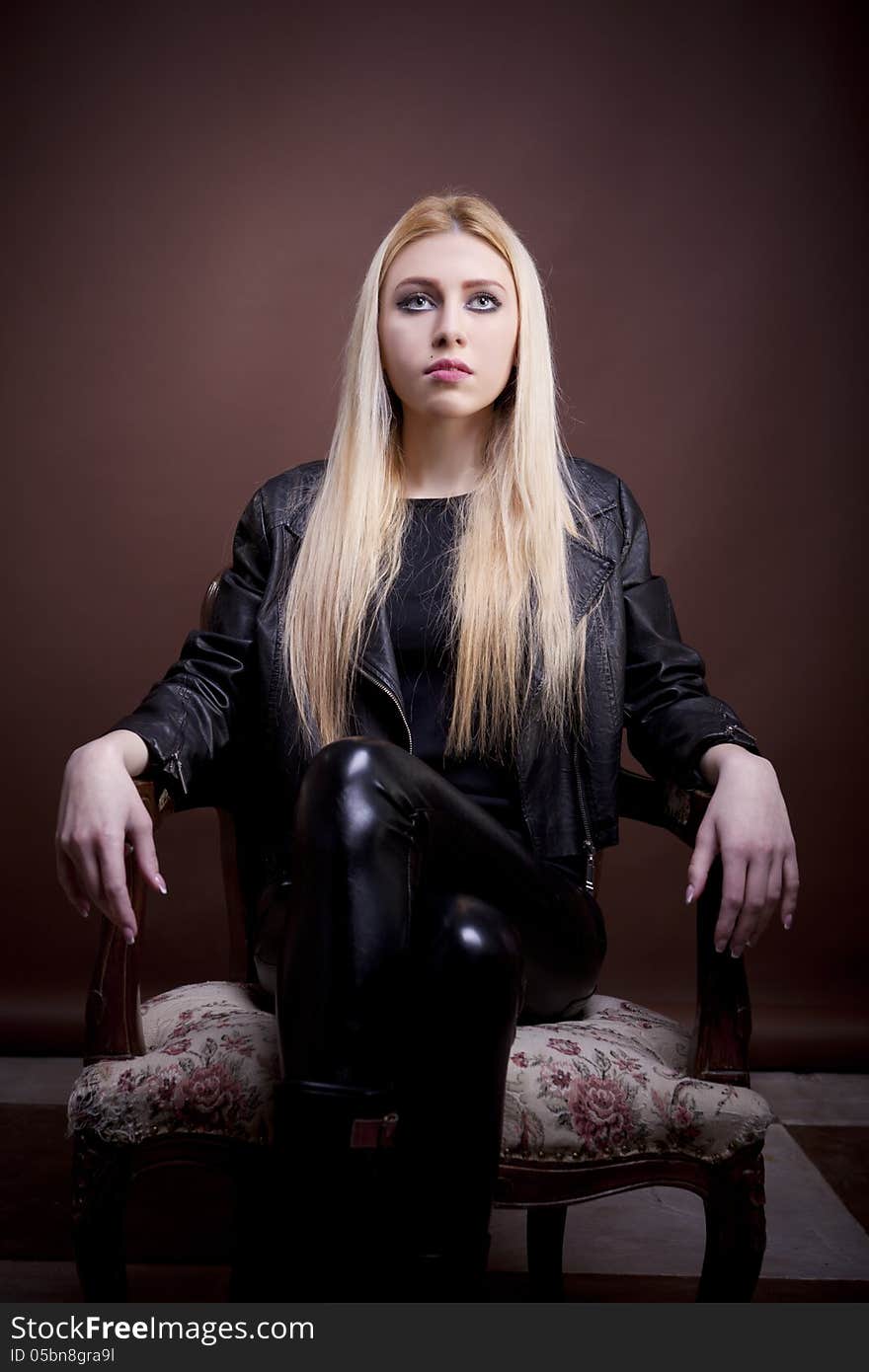 Beautiful girl in leather jacket on a vintage chair looking up studio shot