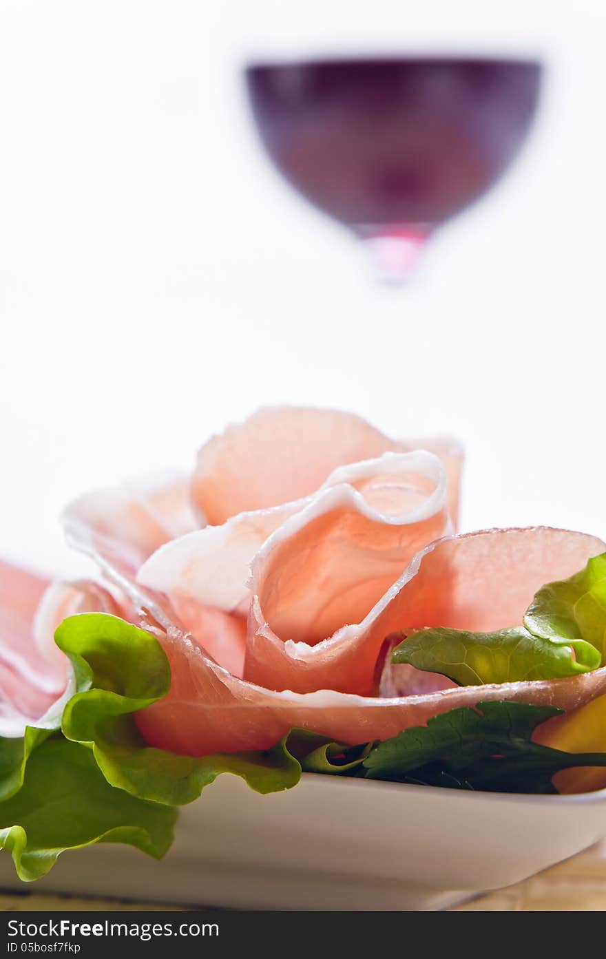 Glass with red wine and ham with salad , focus on a foreground