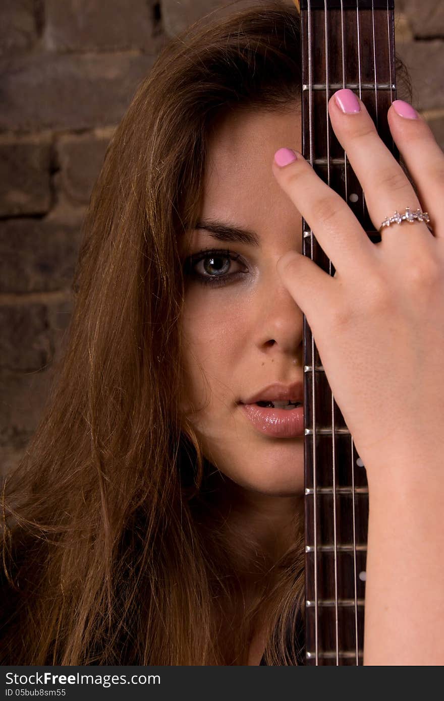 Portrait of a Girl. In the foreground, neck of the guitar. In the background a brick wall. Portrait of a Girl. In the foreground, neck of the guitar. In the background a brick wall