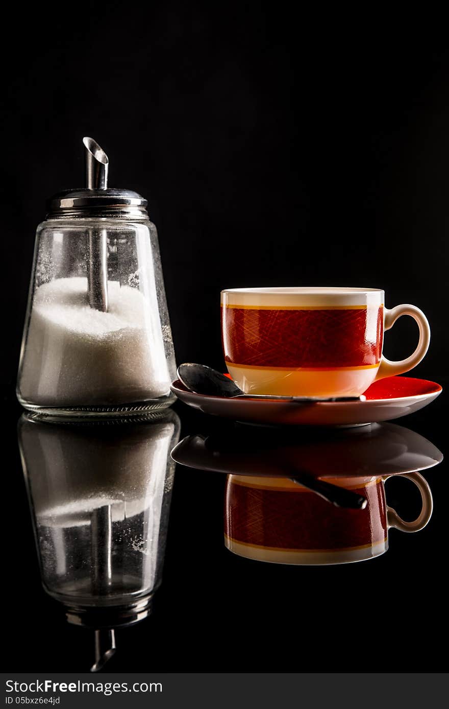 Sugar-basin with white sugar and a cup of tea or coffee on reflecting surface. on black. Shot in studio. Sugar-basin with white sugar and a cup of tea or coffee on reflecting surface. on black. Shot in studio