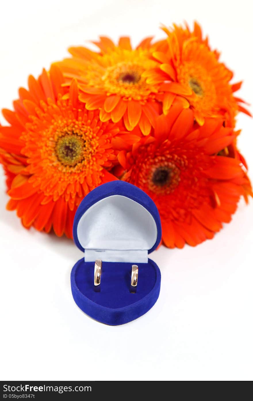 Two gold wedding rings with a bouquet of orange gerberas