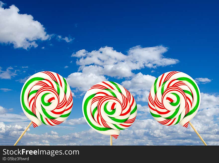 Sugar lollipops in white green and red on background of sky and clouds. Sugar lollipops in white green and red on background of sky and clouds