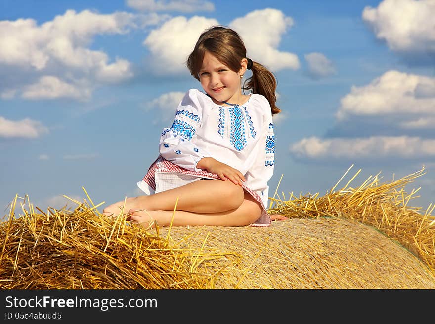 Small rural girl on the straw after harvest field with straw bales