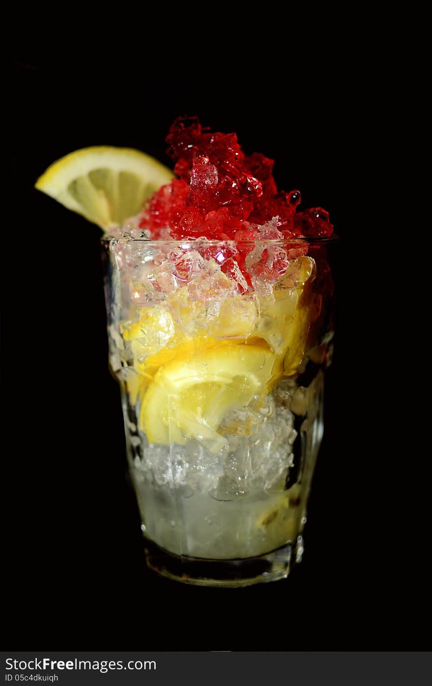 A drink in tall glass with lemon and ice, and red garnish