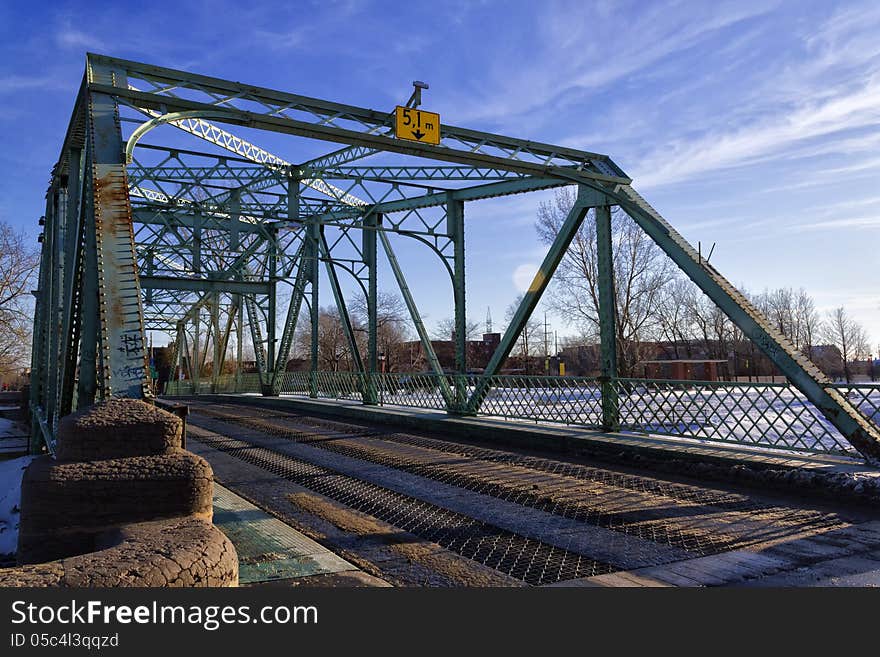 Small steel bridge crossing the canal with winter scenery in the background