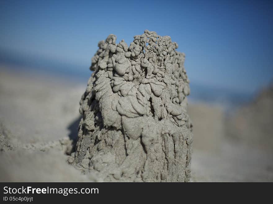 Close up of a sand castle made from dribbled sand. Blue sky in background.