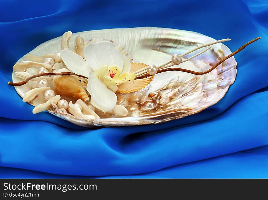 Composition from pearls, coral and orchids on blue background.