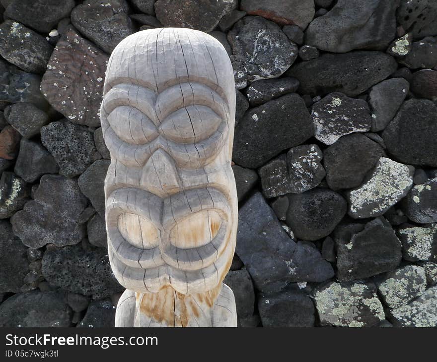 Face of a carved wood tiki statue standing in front of a lava rock wall at Puuhonua O Honaunau Place of Refuge historical park on the big island of Hawaii. Face of a carved wood tiki statue standing in front of a lava rock wall at Puuhonua O Honaunau Place of Refuge historical park on the big island of Hawaii.