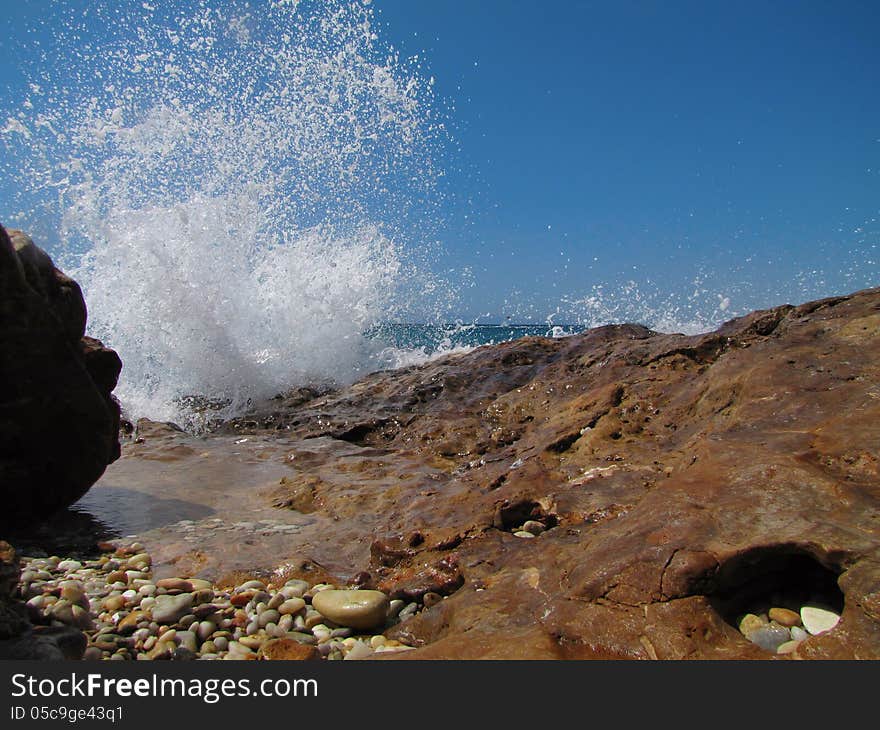 Gravel, wet, rocky coast and splashing waves against clear, blue sky in a sunny day, Thassos Island, Greece. Gravel, wet, rocky coast and splashing waves against clear, blue sky in a sunny day, Thassos Island, Greece