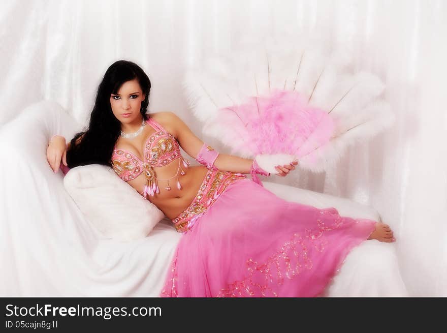 Portrait of beautiful bellydancer wearing a light pink costume and holding a pink and white feather fan. She is seated in a reclined position. Portrait of beautiful bellydancer wearing a light pink costume and holding a pink and white feather fan. She is seated in a reclined position.