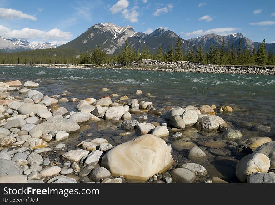 Selective focus on the rocks in the foreground with mountains in the background at Snaring River located in Jasper National Park, Alberta, Canada. Selective focus on the rocks in the foreground with mountains in the background at Snaring River located in Jasper National Park, Alberta, Canada.