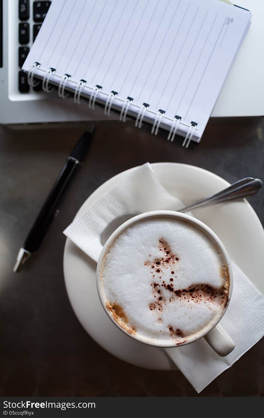 A cup of coffee ,notepad and a laptop on a desk