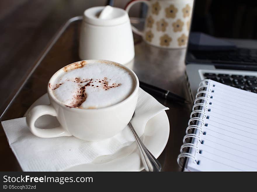 A cup of coffee ,notepad and a laptop on a desk