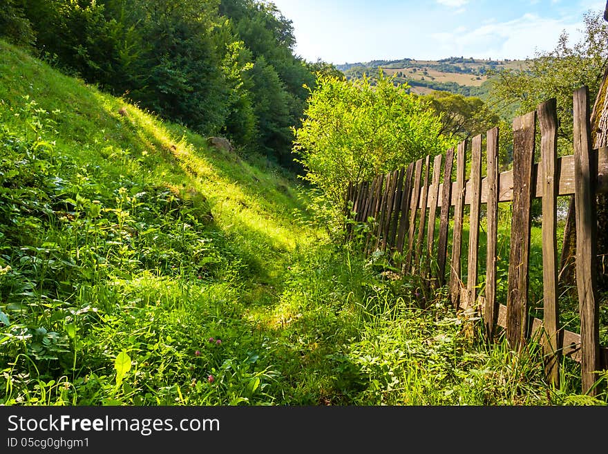 Wooden stick fence in village in mountains with blue sky, green grass and path in good weather time. Wooden stick fence in village in mountains with blue sky, green grass and path in good weather time