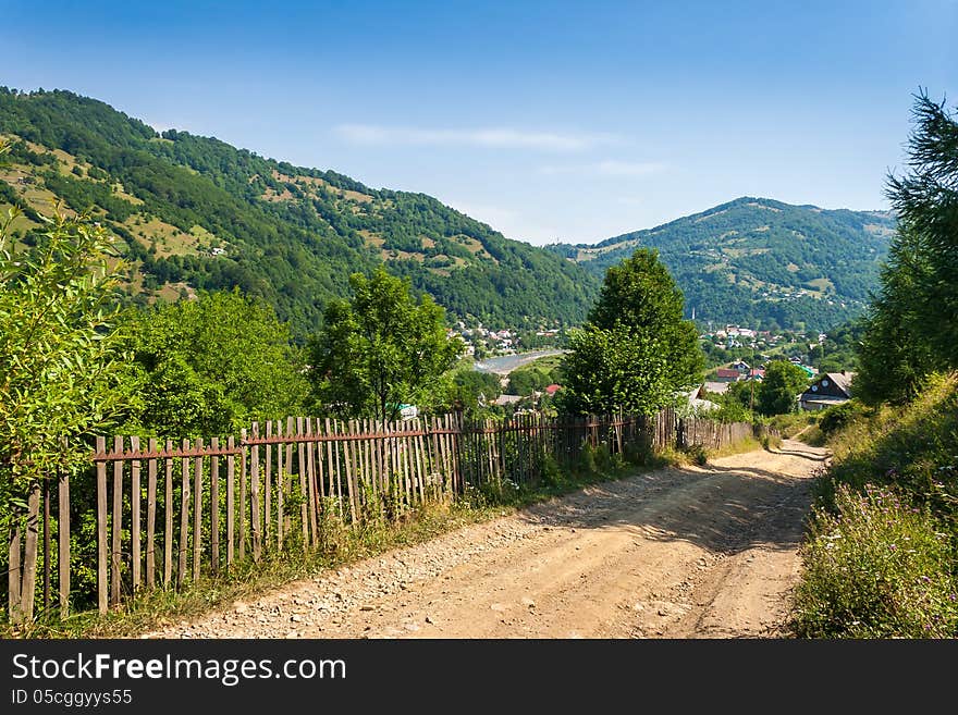 Wooden stick fence in village in mountains with blue sky, green grass and path in good weather time. Wooden stick fence in village in mountains with blue sky, green grass and path in good weather time