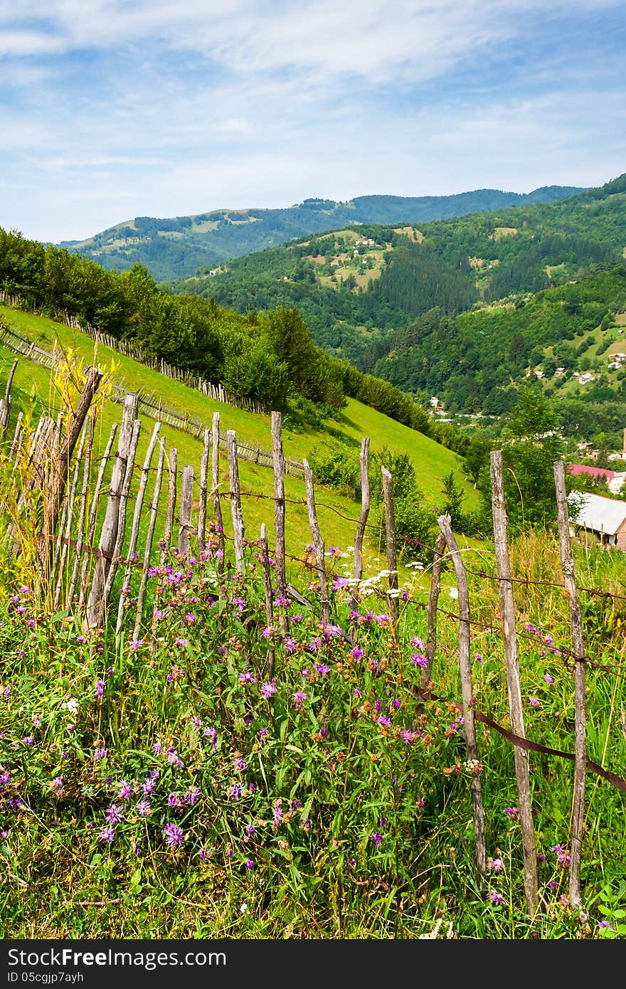 Wooden stick fence in village in mountains with blue sky, green grass and path in good weather time. Wooden stick fence in village in mountains with blue sky, green grass and path in good weather time