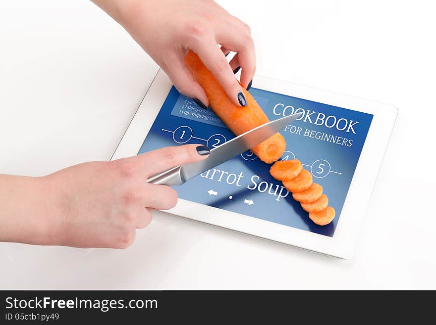 Women's hands is cutting the carrot on a tablet computer, on which there is a recipe of carrot soup. Women's hands is cutting the carrot on a tablet computer, on which there is a recipe of carrot soup.