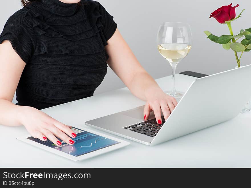 A business woman is working with the modern laptop and tablet computer. Nearby on the table is a glass of wine and one rose. A business woman is working with the modern laptop and tablet computer. Nearby on the table is a glass of wine and one rose.