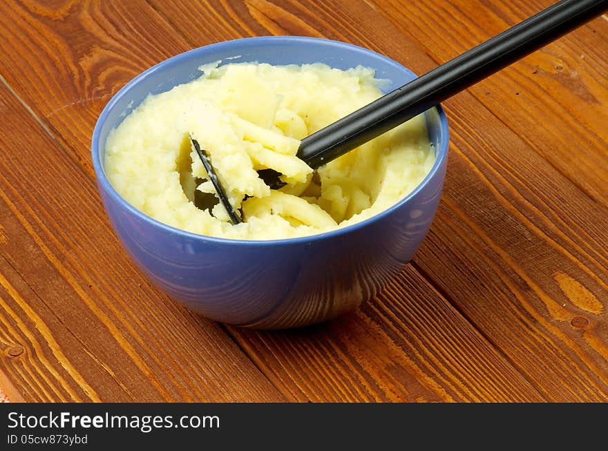 Tasty Mashed Potato with Potato Masher in Blue Bowl on Wooden background