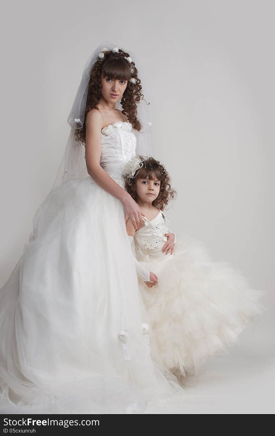 Full-length portrait of harmonious girl in a luxurious wedding dress with a cute little girl on a white background in the studio. Full-length portrait of harmonious girl in a luxurious wedding dress with a cute little girl on a white background in the studio