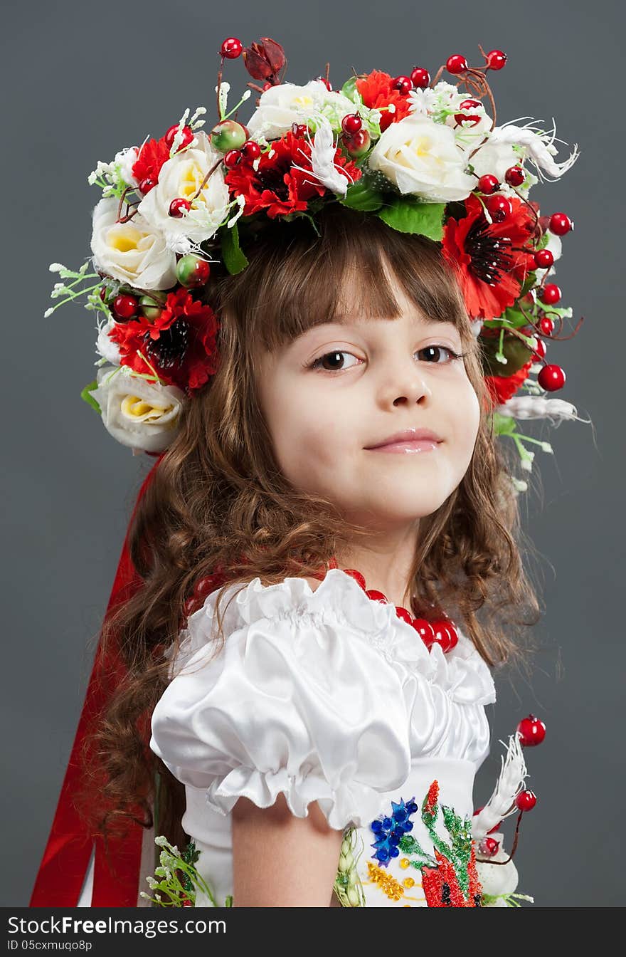 Close-up portrait of cute little girl dressed in folk costumes with large bright wreath on her head on gray background in the studio. Close-up portrait of cute little girl dressed in folk costumes with large bright wreath on her head on gray background in the studio