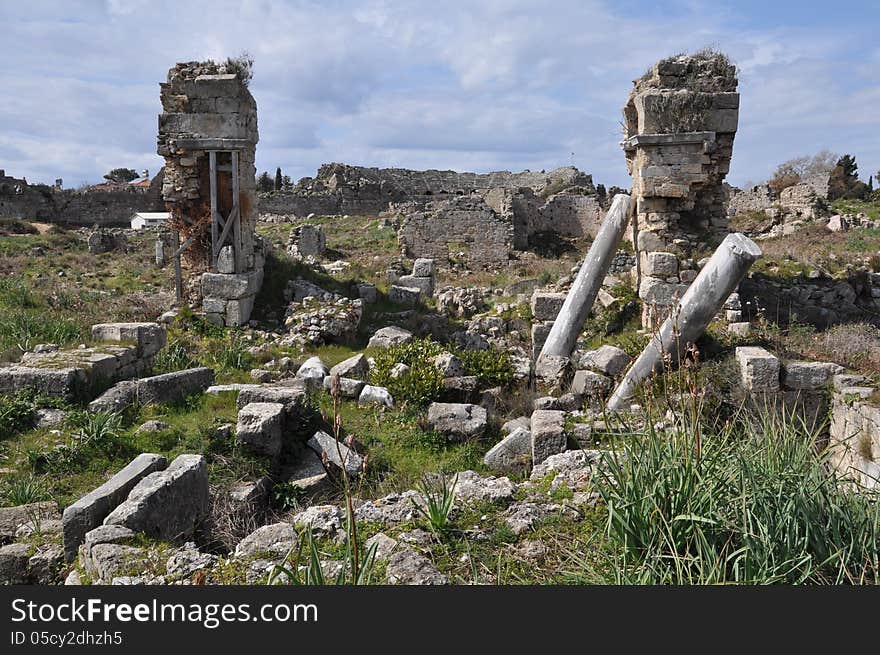 Image shows details of Antique Side, Turkey. Image is dominated by ruins in the front and in the amphitheatre in the middle. Sky is blue and light cloudy. Image shows details of Antique Side, Turkey. Image is dominated by ruins in the front and in the amphitheatre in the middle. Sky is blue and light cloudy.