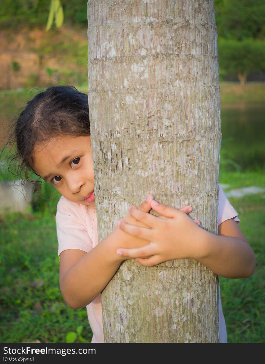 A cute girl is behind a tree under sunlight