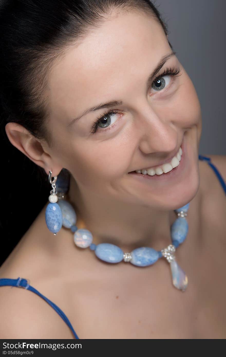 Close up portrait of young happy smiling woman wearing earrings and necklace of light blue stones. Natural beauty face. Selective focus. Shot in studio. Close up portrait of young happy smiling woman wearing earrings and necklace of light blue stones. Natural beauty face. Selective focus. Shot in studio.