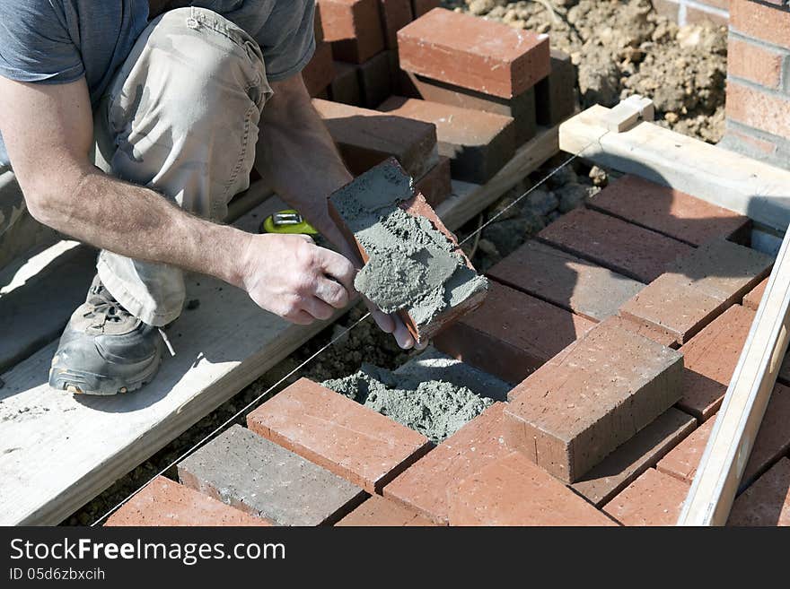 This is an image of a brick mason applying mortar to a brick before setting the brick in place. This is an image of a brick mason applying mortar to a brick before setting the brick in place.