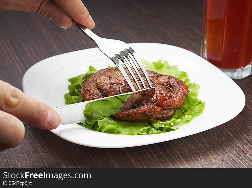 Cutting grilled steak with knife and fork on white plate. Cutting grilled steak with knife and fork on white plate