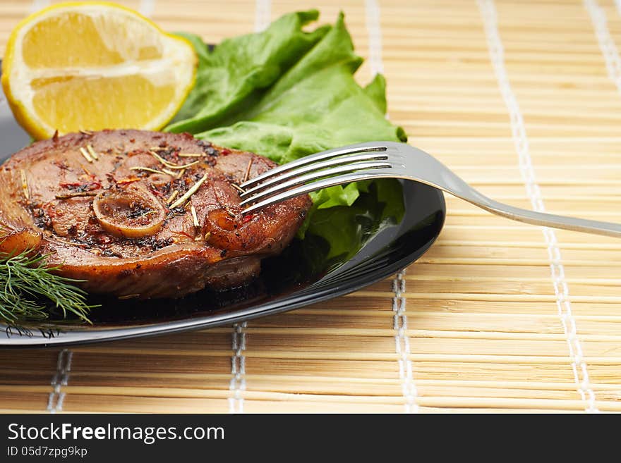 Grilled steak with salad and lemon on black plate with fork