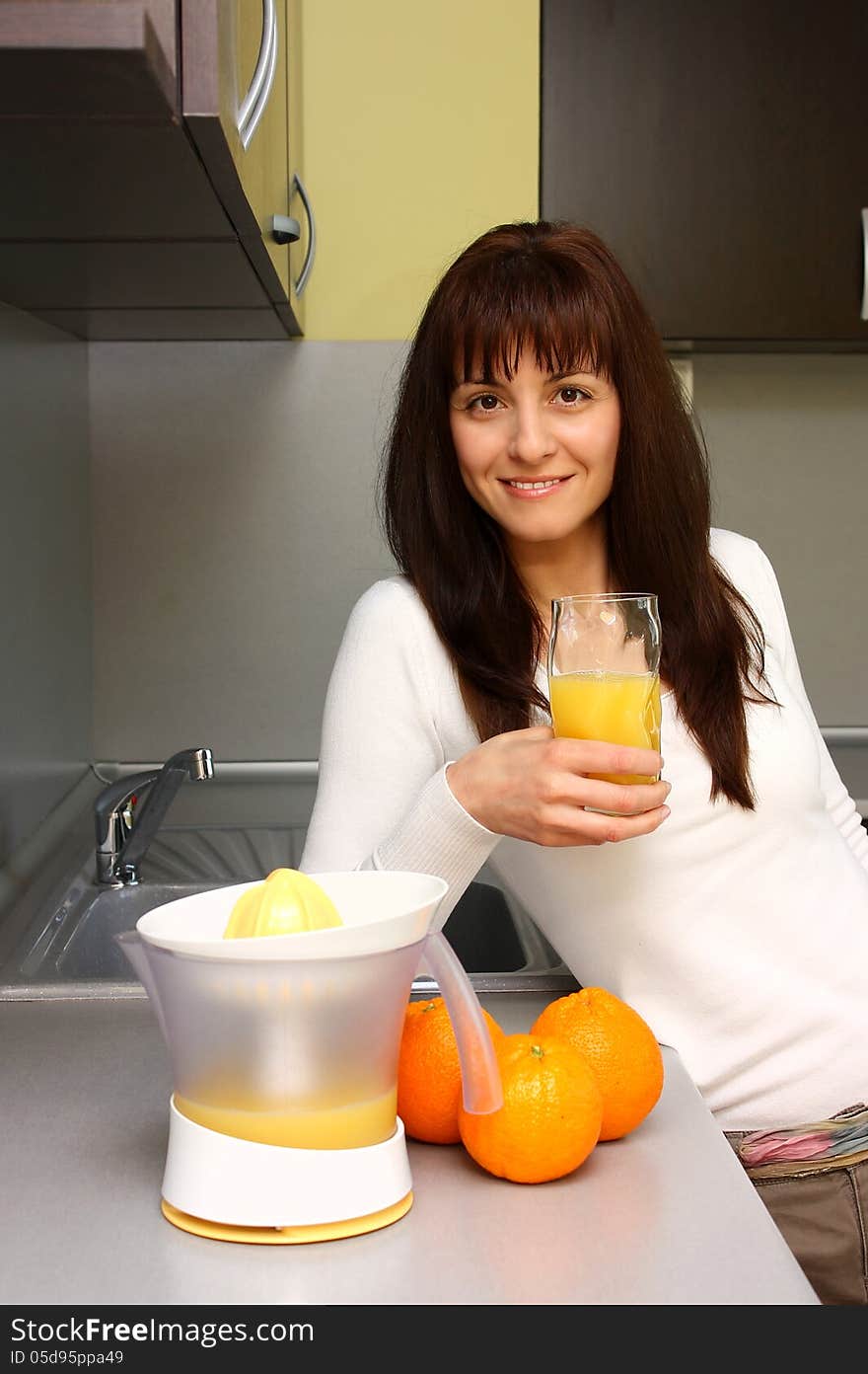 Smiling woman making and drinking orange juice in kitchen. Smiling woman making and drinking orange juice in kitchen