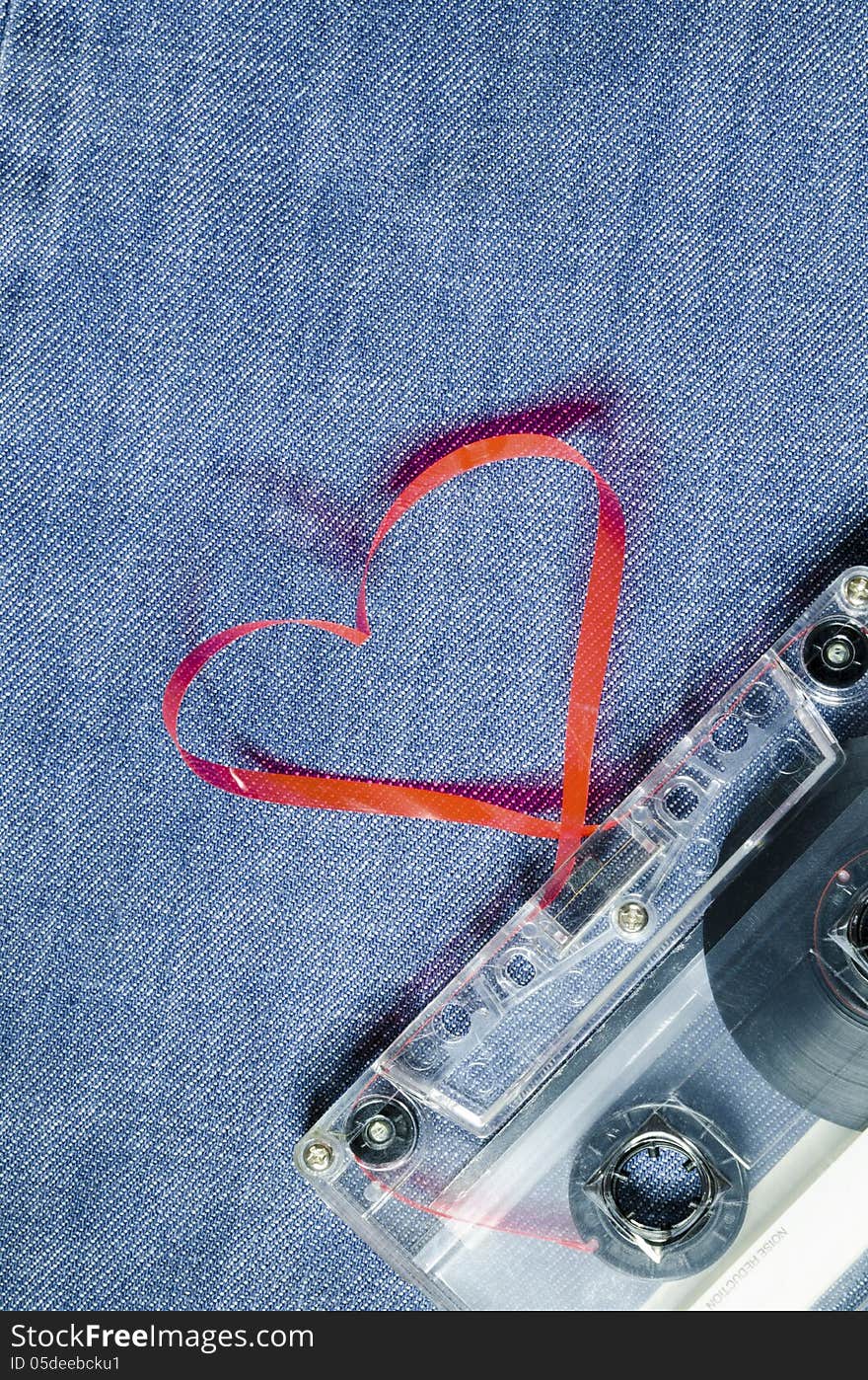 Vintage audio cassette on blue jeans with red tape pulled out as heart shape. Vintage audio cassette on blue jeans with red tape pulled out as heart shape