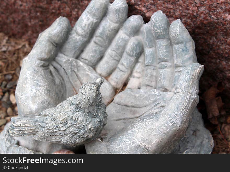 Sculpture of old,weathered stone hands open and holding little bird in palm.