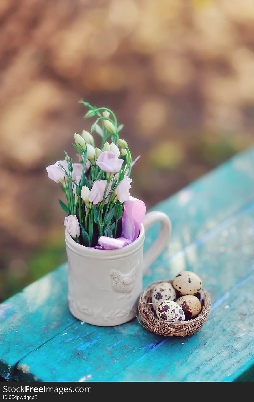 Quail eggs in the nest and a cup with flowers on a blue bench. Quail eggs in the nest and a cup with flowers on a blue bench