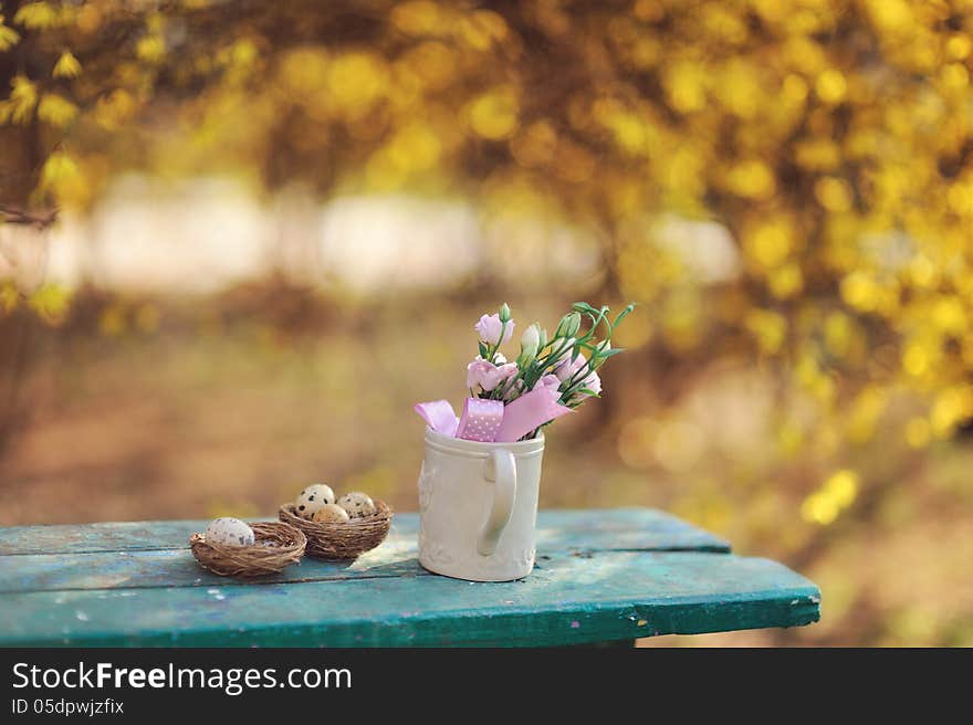 Quail eggs in the nest and a cup with flowers on a blue bench. Quail eggs in the nest and a cup with flowers on a blue bench