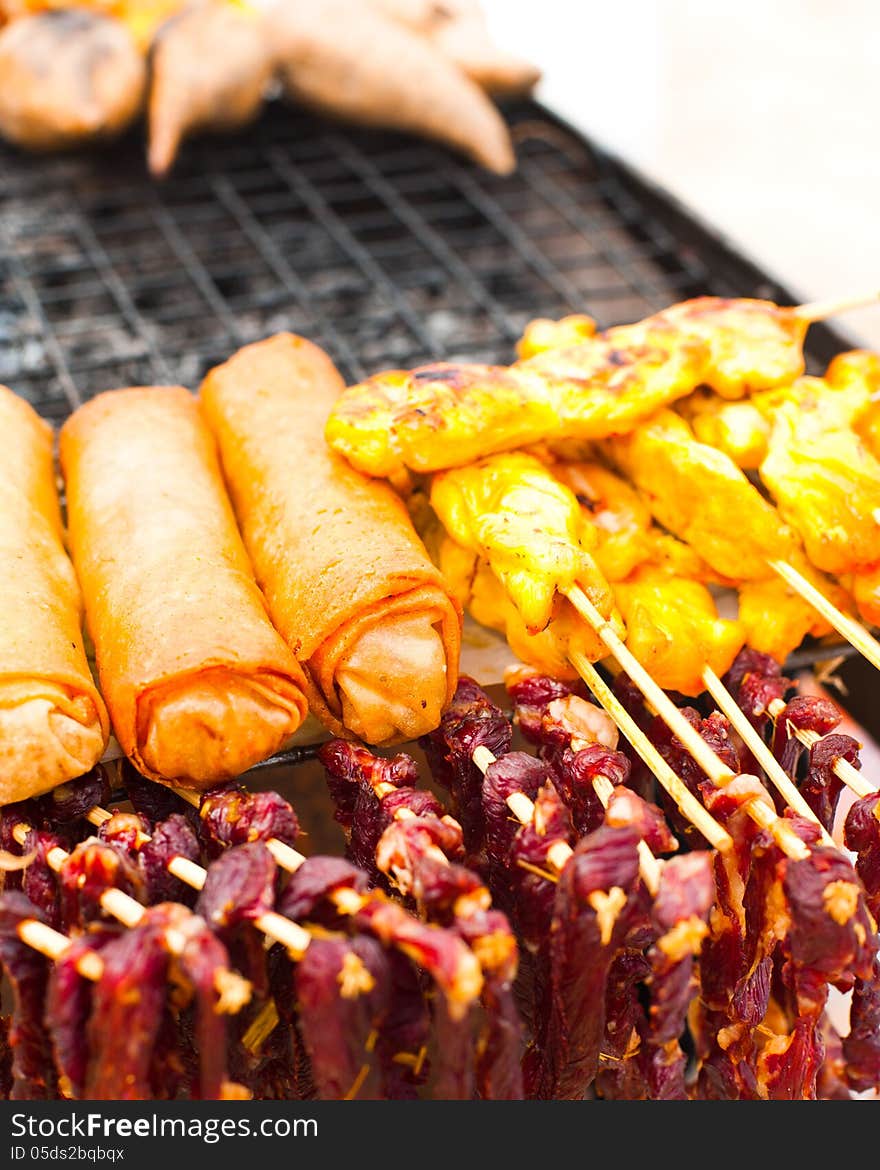 Traditional Thai food at market. Dry beef meat, spring rolls and curry chicken on grill