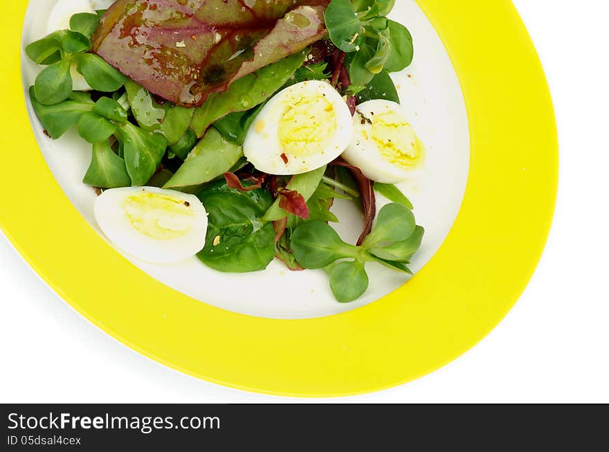 Salad with Greens, Chard, Quail Eggs and Corn Salad on Yellow Plate closeup on white background. Salad with Greens, Chard, Quail Eggs and Corn Salad on Yellow Plate closeup on white background