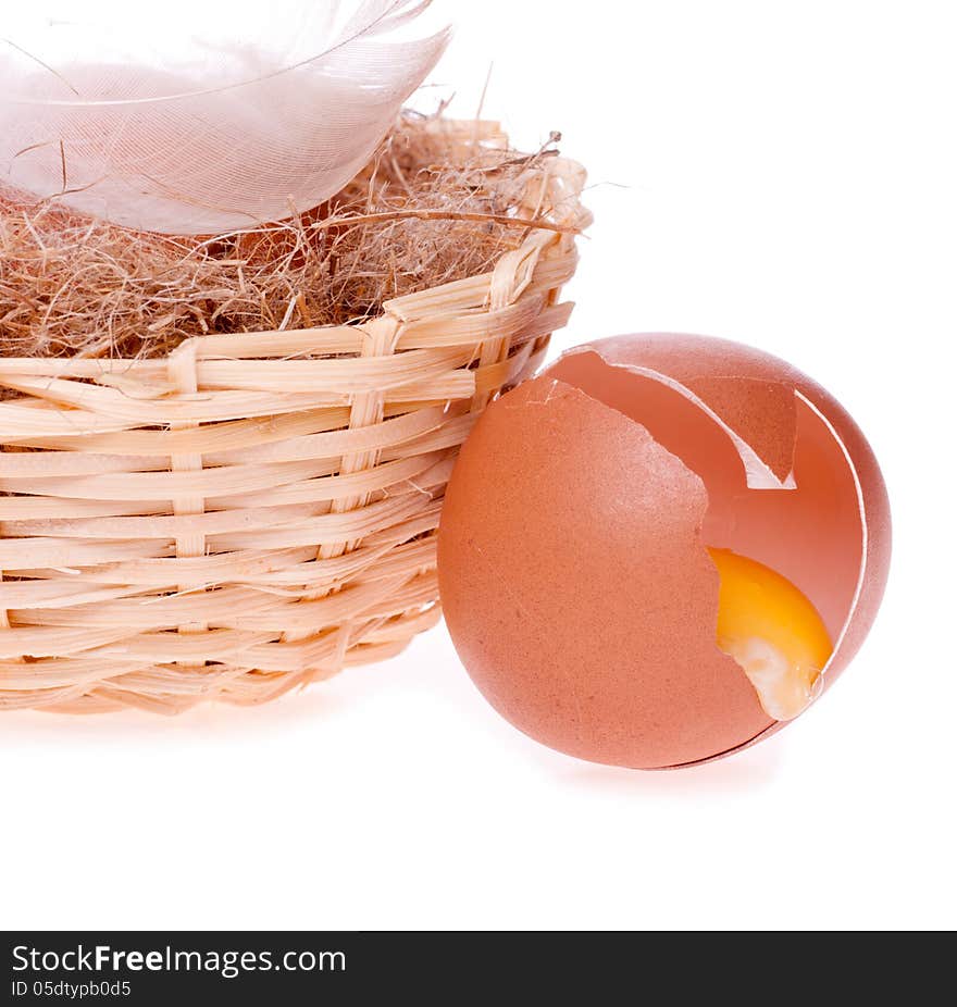 Egg broken on the background of nests with egg and the feather of a bird on the white