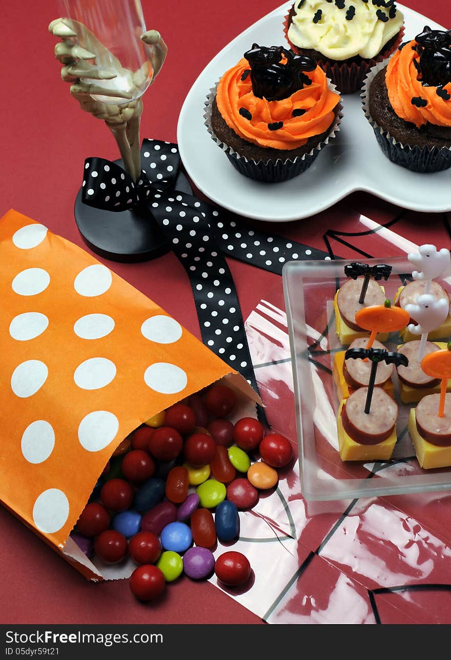 Happy Halloween party table with skeleton glass, cupcakes, candy lollies and party food with orange and black pumpkin, cat, bat and ghost decorations. Happy Halloween party table with skeleton glass, cupcakes, candy lollies and party food with orange and black pumpkin, cat, bat and ghost decorations.