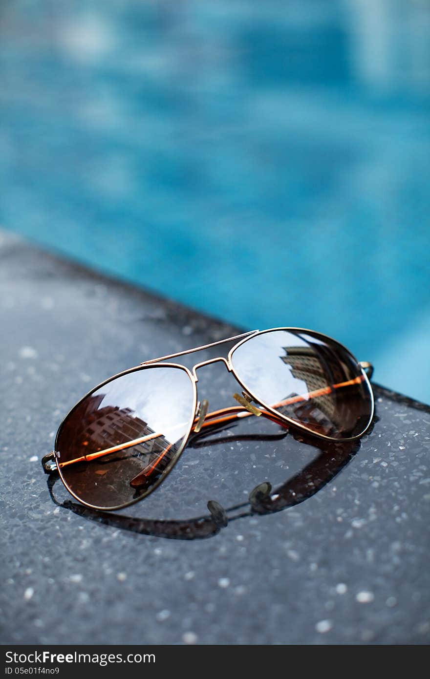 Sunglasses by a blue pool in city town on holiday. Sunglasses by a blue pool in city town on holiday