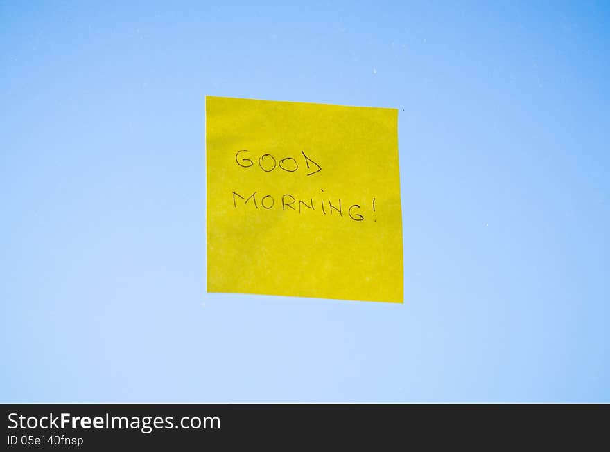 Good Morning text handwritten on a sticky note against blue background