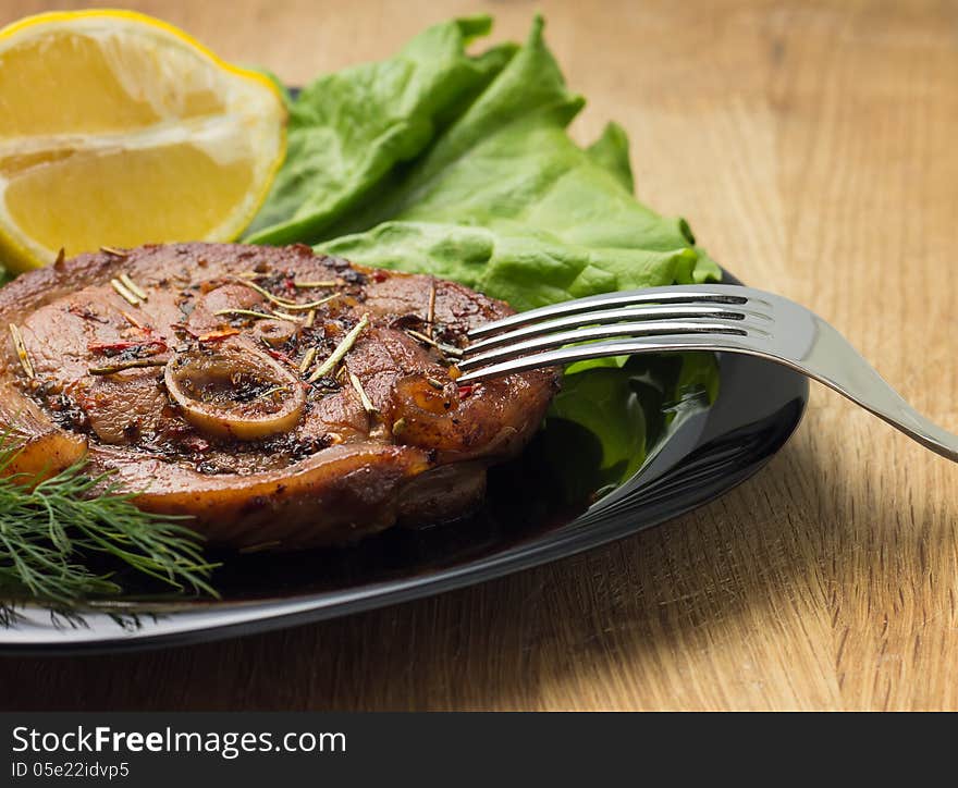 Grilled steak with salad and lemon at black plate with fork on wood background. Grilled steak with salad and lemon at black plate with fork on wood background