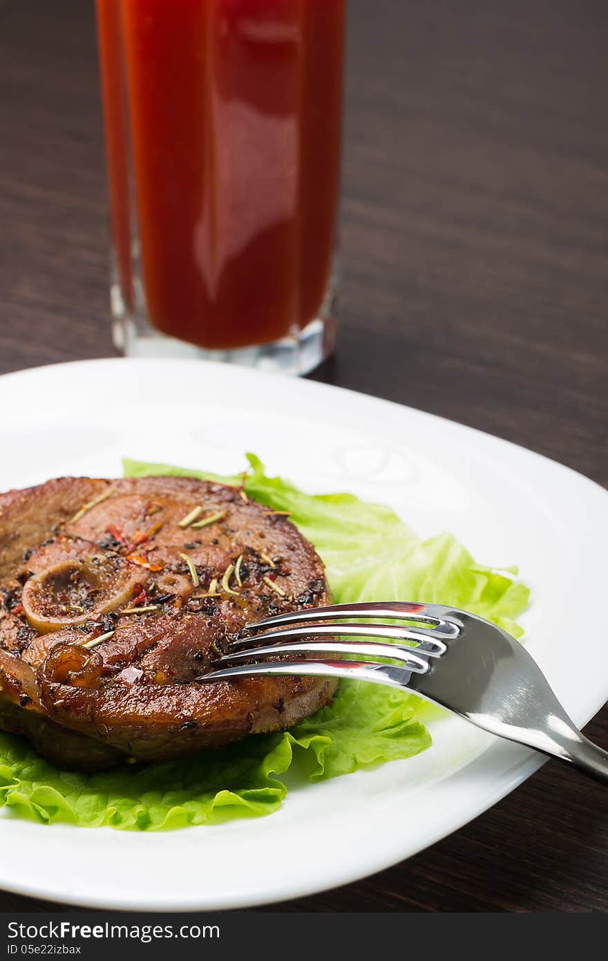 Eating grilled steak with knife and fork on white plate with glass of tomato juice