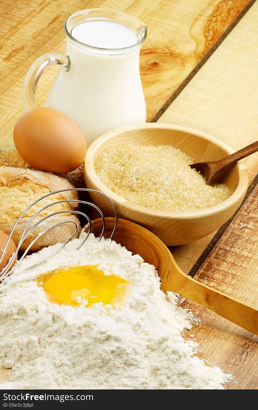 Preparing Dough. Ingredients with Jar of Milk, Flour, Egg, Sugar and Wooden Spoon with Egg Whisk closeup on Wooden background