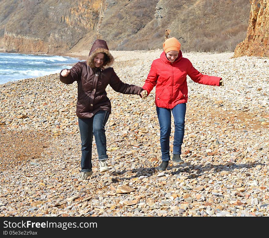 Two girls in red and purple coats jumping on the seashore. Two girls in red and purple coats jumping on the seashore