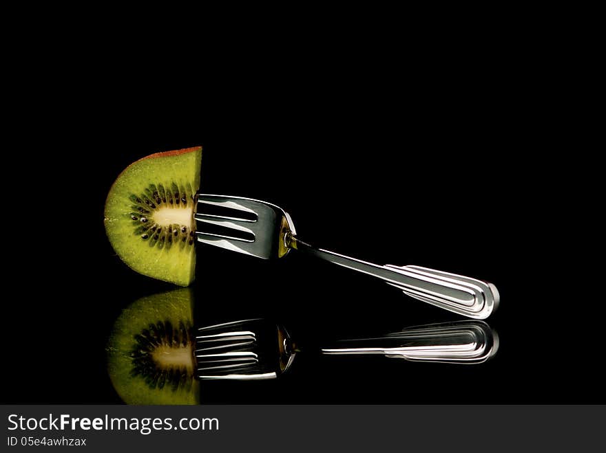 A piece of kiwi fixed on desert fork. Black background. Studio shot.