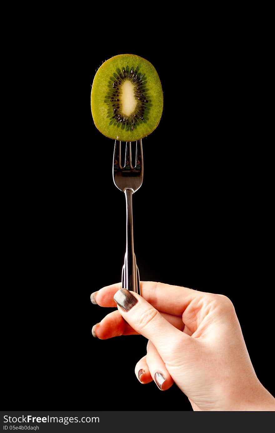 A piece of kiwi fixed on desert fork. Black background. Studio shot.